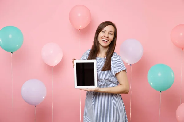 カラフルな気球とパステル ピンクの背景の空白の空の画面とタブレット コンピューターを保持している青いドレスを着てうれしそうな魅惑的な若い女性の肖像画 誕生日休日党概念 — ストック写真