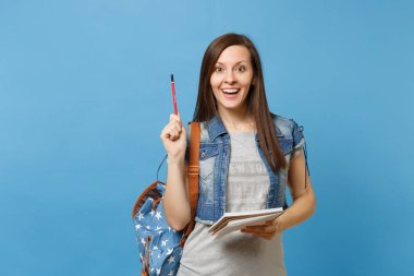 Sırt çantası holding defter ile denim giysili genç oldukça heyecanlı kadın öğrenci portresi, kalem yukarıyı üzerinde mavi arka plan izole. Lise Üniversite kavramı kolej eğitim
