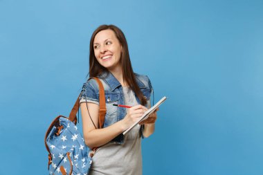 Bir kenara üstünde defter üzerinde mavi arka plan izole Not yazmak sırt çantası arıyorum ile kot elbise genç güzel neşeli kadın öğrenci portresi. Lise Üniversite kavramı kolej eğitim
