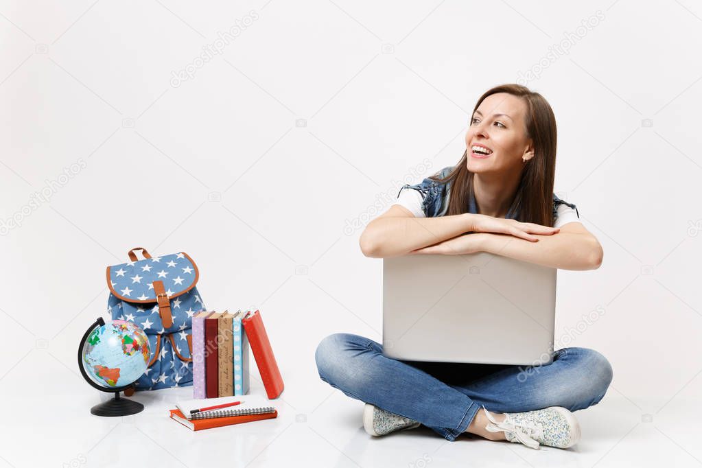 Young joyful laughing woman student leaning on laptop pc computer looking aside sitting near globe,backpack, school books isolated on white background. Education in high school university college.