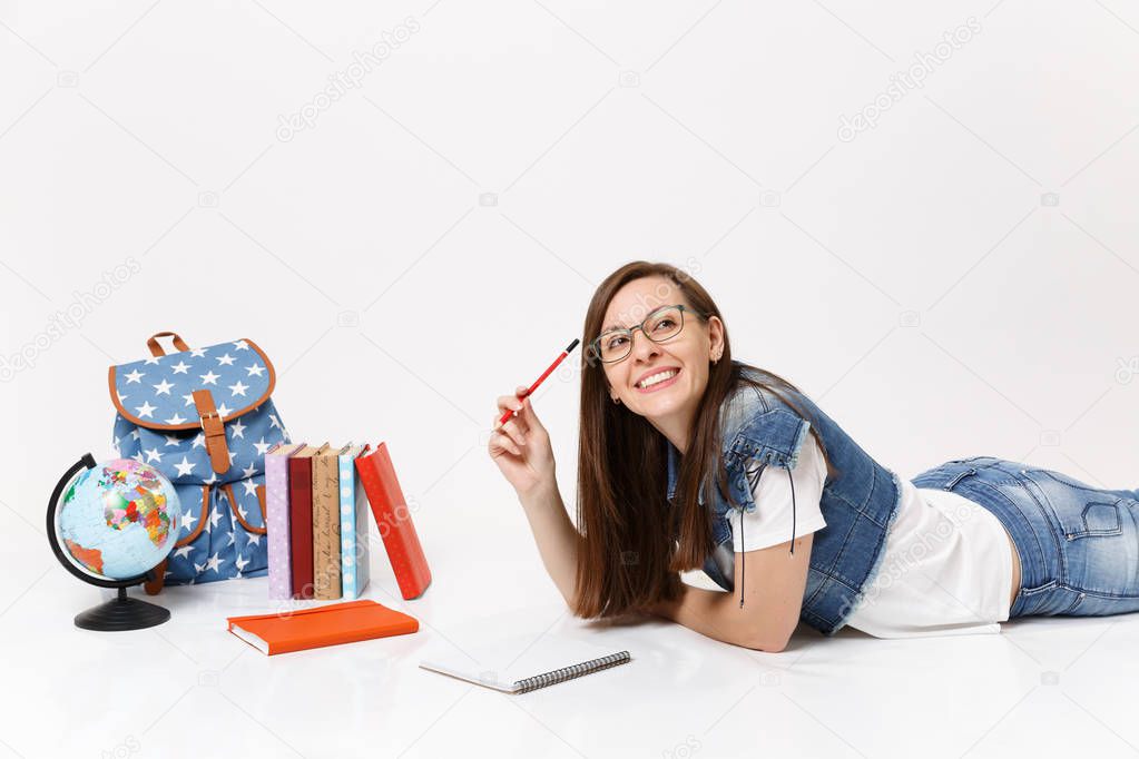 Young joyful pretty woman student in denim clothes, glasses holding pencil notebook lying near globe, backpack, school books isolated on white background. Education in high school university college