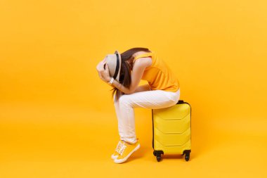 Yazlık kıyafetleri içinde üzgün turist kadın çantanın üstüne oturur sarı turuncu arka planda izole edilmiş kafaya dokunur. Hafta sonları yurtdışına seyahat eden bir kadın. Hava yolculuğu konsepti