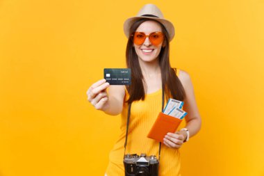 Mutlu turist kadın yaz rahat kıyafetler, kredi kartı, passport biletleri sarı turuncu arka plan üzerinde izole holding şapkası. Hafta sonu kaçış üzerinde seyahat için yurt dişi. Hava uçuş kavramı