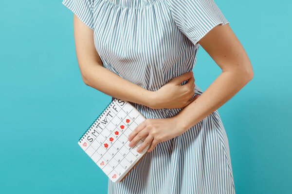 Cropped shot sickness woman in blue dress holding periods calendar for checking menstruation days put hand on tummy isolated on blue background. Medical, healthcare, gynecological concept. Copy space