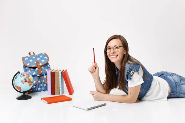 Young smiling pretty woman student in denim clothes, glasses holding pencil notebook lying near globe, backpack, school books isolated on white background. Education in high school university college
