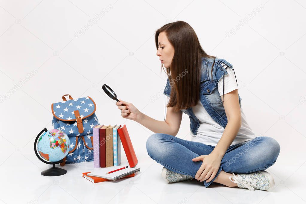 Young curious smart woman student in denim clothes sitting looking on globe, backpack, school books with magnifying glass isolated on white background. Education in high school university college