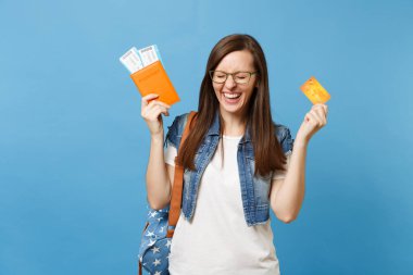 Genç kadın öğrenci sırt çantası ile kapalı gözler passport boarding pass biletleri, kredi kartı üzerinde mavi arka plan izole holding ile çok memnun. Yurt dışındaki üniversiteler eğitim. Hava seyahat uçuş