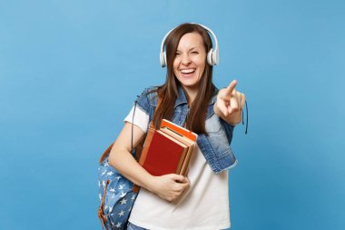 Neşeli kadın öğrenci müzik dinleme sırt çantası kulaklık ile gülen genç okul kitap işaret parmağı üzerinde mavi arka plan izole kamera tutun. Eğitimde yüksek okul üniversiteler