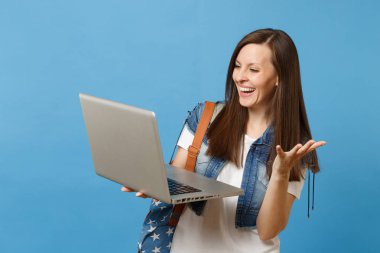 Genç gülmek kadın öğrenci denim giysileri sırt çantası ile tutun çalışma üzerinde mavi arka plan izole eller yayılan dizüstü pc bilgisayar kullanma. Üniversitesi'nde eğitim. Kopya alanı reklam için