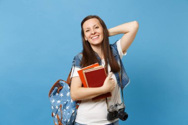 Sırt çantası ve retro vintage fotoğraf makinesi boynundaki el üzerinde kafa tutmak ile genç neşeli kadın öğrenci okul kitapları üzerinde mavi arka plan izole tutun. Lise Üniversite kavramı kolej eğitim