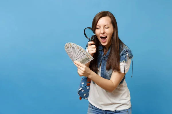 怪しい女で若い学生のバックパックを探してドルのバンドル多くの青の背景に分離された紙幣をチェック虫眼鏡で現金お金 お金の正当性を検証 — ストック写真