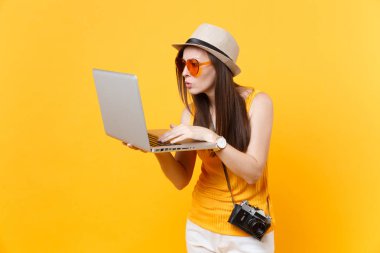 Üzgün üzgün turist kadın yaz rahat giysileri, dizüstü pc bilgisayar holding şapkası sarı turuncu arka plan üzerinde izole. Hafta sonu kaçış üzerinde seyahat için yurt kız. Hava uçuş yolculuk kavramı