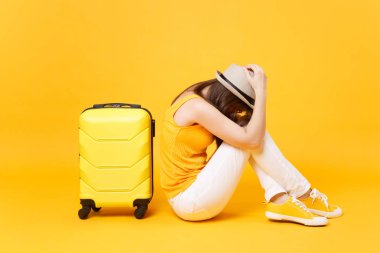 Üzgün gezgin turist kadın yaz rahat kıyafetler, sarı turuncu arka plan üzerinde izole bavul yakınındaki şapka sit. Hafta sonu kaçış üzerinde seyahat için yurt kadın yolcu. Hava uçuş kavramı