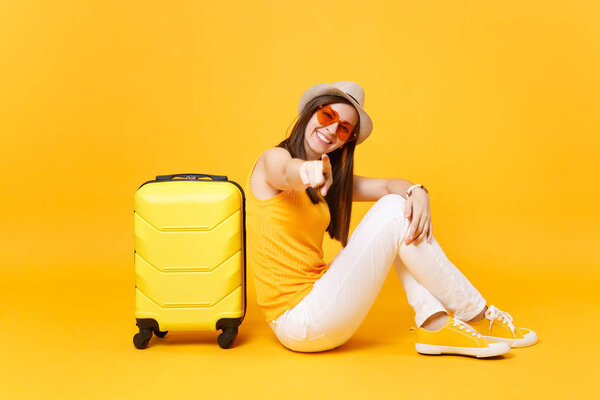Traveler tourist woman in summer casual clothes, hat sit with suitcase isolated on yellow orange background. Female passenger traveling abroad to travel on weekends getaway. Air journey concept
