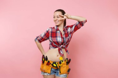 Giyen ekose gömlek, kot şort, kit araçları kemer, pembe arka plan izole çeşitli yararlı araçların tam güçlü genç tamirci kadın. Kadın erkek işi. Yenileme ve işgal kavramı