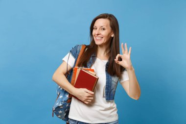 Denim giysileri Ok işaret gösteren ve okul kitapları üzerinde mavi arka plan izole tutmak sırt çantası ile genç casual gülümseyen kadın öğrenci portresi. Lise Üniversite kavramı kolej eğitim