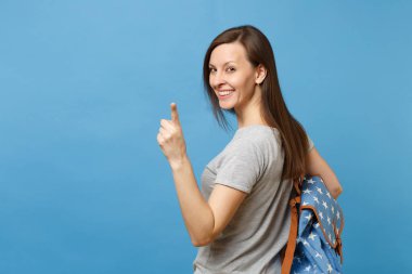 İşaret parmağı üzerinde mavi arka plan izole kamera seyir sırt sırt çantası ile Dikiz genç çekici esmer kadın öğrenci geri. Üniversitede eğitim. Kopya alanı reklam için