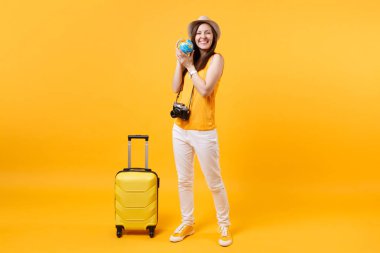 Seyahat etmek turist kadın yaz rahat kıyafetler, küre, sarı turuncu arka plan üzerinde izole bavul ile şapka. Hafta sonu kaçış üzerinde seyahat için yurt dışında seyahat yolcu. Hava uçuş yolculuk kavramı
