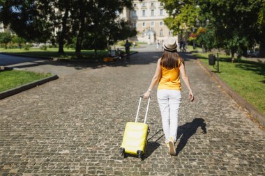 Dikiz seyahat etmek turist kadın sarı yaz rahat kıyafetler şapkalı şehirde açık bavul dönüyoruz. Hafta sonu kaçış üzerinde seyahat için yurt kız. Turizm yolculuk yaşam tarzı kavramı