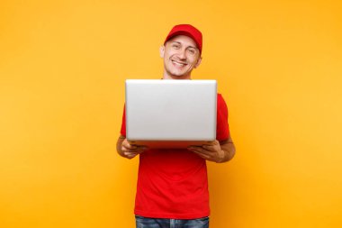 Sarı turuncu arka plan üzerinde izole teslimatçı. Profesyonel erkek çalışan kurye kırmızı şapkalı, dizüstü pc bilgisayarda yazarak çalışma tutan t-shirt. Hizmet anlayışı. Kopya alanı reklam için
