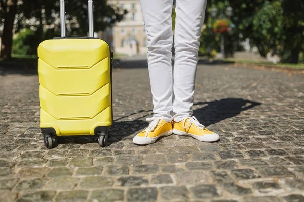 Cropped image of traveler tourist woman legs in yellow summer casual clothes with suitcase on road in city outdoor. Girl traveling abroad to travel on weekends getaway. Tourism journey lifestyle