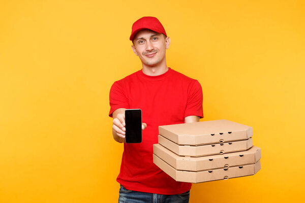Delivery man in red cap t-shirt giving food order italian pizza in flatbox boxes on yellow background. Male employee pizzaman courier hold mobile phone with blank empty screen mockup. Service concept