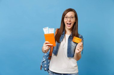 Genç kadın öğrenci sırt çantası ile açılan ağzı pasaport yatılı pas bilet kredi üzerinde mavi arka plan izole kart tutan şaşırttı. Yurt dışındaki üniversiteler eğitim. Hava seyahat uçuş