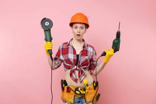 精力充沛的女工在手套 保护性橙色头盔 工具箱工具带充满电力锯电动钻在粉红色的背景上隔离 女性在男性工作 装修理念 — 图库照片