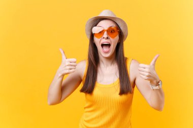 Başparmak yukarıya, sarı zemin üzerine izole kopya alanı gösterilen saman yaz şapka, turuncu gözlük çok memnun gülen genç kadın portresi. İnsanlar samimi duygular yaşam tarzı kavramı. Reklam alanı