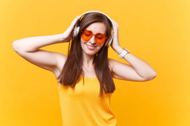 Turuncu gözlük üzerinde sarı arka plan izole kulaklık kopya alanı içinde müzik dinlemek sakin gülümseyen genç kadın portresi. İnsanlar samimi duygular, yaşam kavramı. Reklam alanı. Geri kalan sakin ol