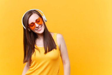 Turuncu gözlük üzerinde sarı arka plan izole kulaklık kopya alanı içinde müzik dinlemek sakin gülümseyen genç kadın portresi. İnsanlar samimi duygular yaşam tarzı kavramı. Reklam alanı. Dinlenmek, dinlenmek