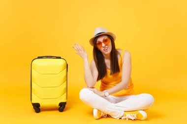 Sıkılmış turist kadın yaz rahat kıyafetler şapkalı bavulla otur, sarı turuncu arka plan üzerinde izole uçak için bekleyin. Hafta sonu kaçış üzerinde seyahat için yurt kız. Hava uçuş kavramı