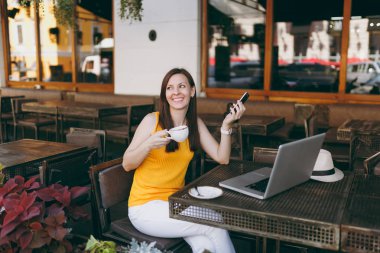 Mutlu kız açık havada sokak kafe kafede dizüstü pc bilgisayar masasi, manifatura ileti cep telefonu, fincan çay içmek serbest zaman sırasında restoranda oturan. Mobil ofis serbest kavramı