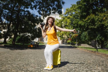Seyahat etmek turist kadın retro vintage fotoğraf kamera Yayilim şehirde açık elele bavula oturan şapkalı çok memnun. Hafta sonu kaçamağı yurt kız. Turizm yolculuk yaşam tarzı