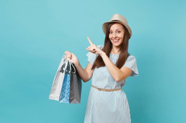 Moda gülümseyen güzel beyaz kadın portre yaz elbise, hasır şapka alışveriş izole mavi pastel arka plan üzerinde sonra paketleri çanta satın almalarla tutarak. Kopya alanı reklam için