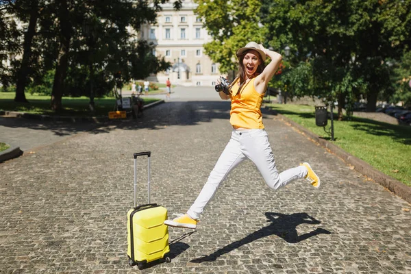 若者は レトロなビンテージ写真カメラ市屋外にジャンプを保持を叫んでスーツケースと帽子の旅行観光女を大喜び 週末の休暇に海外旅行の女の子 観光旅ライフ スタイル — ストック写真