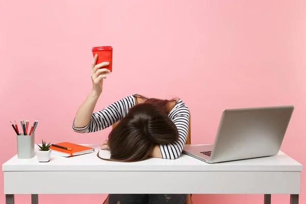 Yorgun kadın oturup, kahve veya çay tablo holding bardakta kafasını koyduğu pastel pembe arka plan üzerinde izole pc dizüstü bilgisayar ile beyaz masa başında çalışmak. Başarı iş kariyer kavramı. Kopya alanı