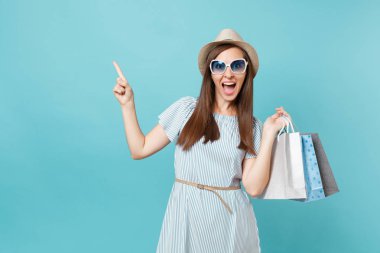 Moda çekici mutlu kadın portre yazlık elbise, hasır şapka, güneş gözlüğü izole mavi pastel arka plan üzerinde alışveriş sonra paketleri çanta satın almalarla tutarak. Kopya alanı reklam için