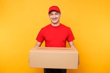 Teslimatçı sarı turuncu arka plan üzerinde izole kırmızı üniforma. Profesyonel erkek çalışan kurye veya Bayi kap t-shirt boş karton kutu tutarak. Paket hizmet anlayışı alma.