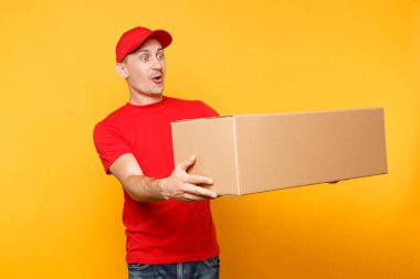 Teslimatçı sarı turuncu arka plan üzerinde izole kırmızı üniforma. Profesyonel erkek çalışan kurye veya Bayi kap t-shirt boş karton kutu tutarak. Paket hizmet anlayışı alma.