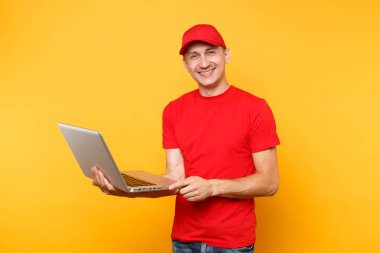 Sarı turuncu arka plan üzerinde izole teslimatçı. Profesyonel erkek çalışan kurye kırmızı şapkalı, dizüstü pc bilgisayarda yazarak çalışma tutan t-shirt. Hizmet anlayışı. Kopya alanı reklam için