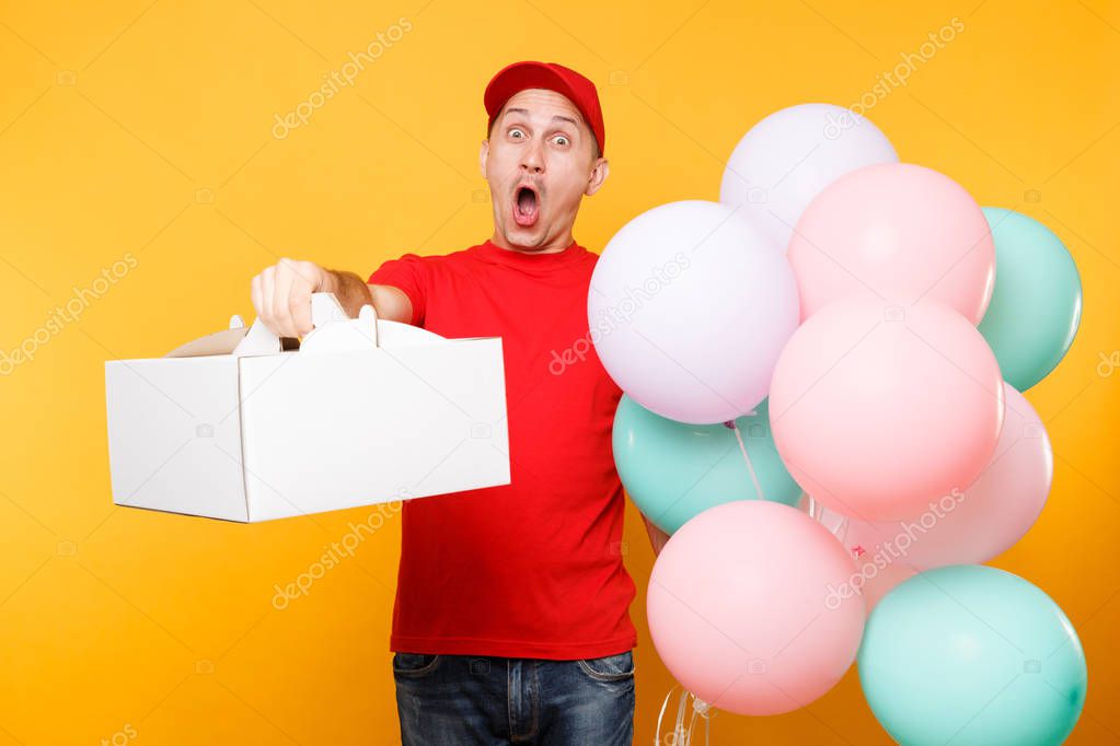 Man giving food order cake box isolated on yellow background. Male employee courier in red cap t-shirt hold colorful air balloons, dessert in empty cardboard box. Delivery service concept. Copy space