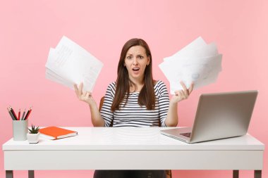 Genç kadın kağıt belgeleri holding, pastel pembe arka plan üzerinde izole dizüstü bilgisayar ile ofiste otururken projede çalışan eller yayılan şaşkın. Başarı iş kariyer kavramı. Kopya alanı