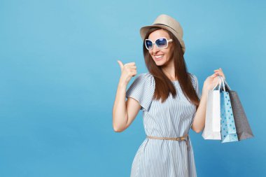 Moda çekici mutlu kadın portre yazlık elbise, hasır şapka, güneş gözlüğü izole mavi pastel arka plan üzerinde alışveriş sonra paketleri çanta satın almalarla tutarak. Kopya alanı reklam için