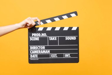 Close up female holding in hand classic director clear empty black film making clapperboard isolated on yellow orange background. Cinematography production concept. Copy space for advertising clipart