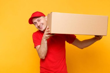 Teslimatçı sarı turuncu arka plan üzerinde izole kırmızı üniforma. Profesyonel erkek çalışan kurye veya Bayi kap t-shirt boş karton kutu tutarak. Paket hizmet anlayışı alma.
