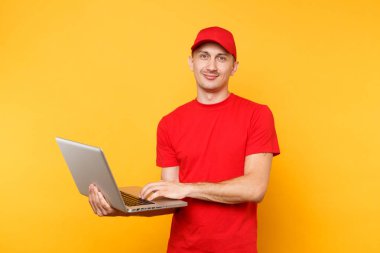 Sarı turuncu arka plan üzerinde izole teslimatçı. Profesyonel erkek çalışan kurye kırmızı şapkalı, dizüstü pc bilgisayarda yazarak çalışma tutan t-shirt. Hizmet anlayışı. Kopya alanı reklam için
