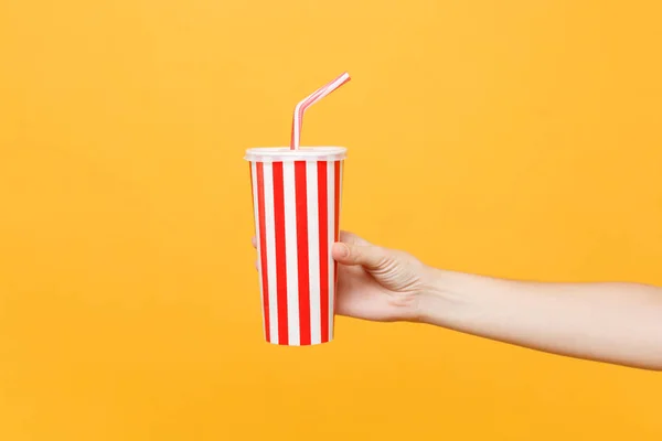Close up female hold in hand classic clear empty striped plastic cup for cola isolated on trending yellow orange background. Cinematography production, takeaway drink concept. Copy space advertising