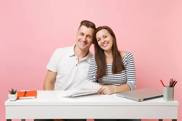 Two young tender business woman man colleagues sit work at white desk with contemporary laptop isolated on pastel pink background. Achievement career concept. Copy space advertising, youth co working