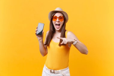 Yaz şapka, turuncu gözlük almak ağız geniş heyecanlı hayran kadın portresi açın, şaşırmış gibisin, boş boş ekran üzerinde sarı arka plan izole cep telefonu tutarsınız. İnsanların duyguları kavramı